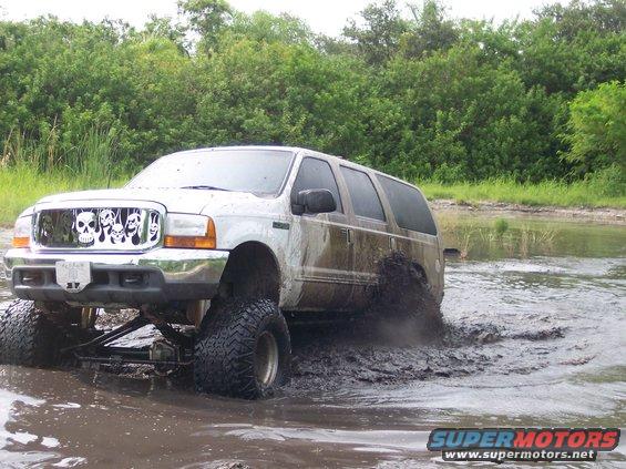 Lifted 2000 Ford Excursion with skull grille driving through mud