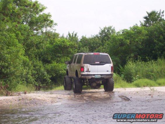 Lifted 2000 Ford Excursion with large tires driving through shallow water