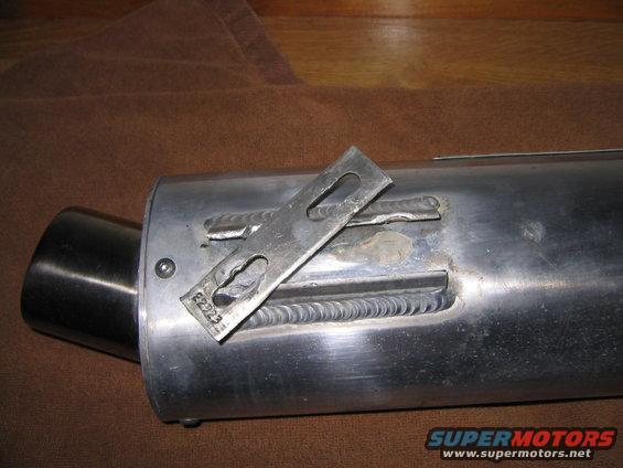 Motorcycle exhaust pipe with metal bracket and visible welds. Part number E2223 is stamped on the bracket