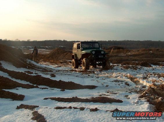 Green Jeep Wrangler parked on snowy dirt mounds with a person standing nearby