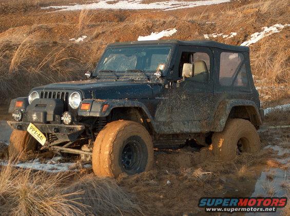Black Jeep Wrangler stuck in mud with large tires and aftermarket bumper
