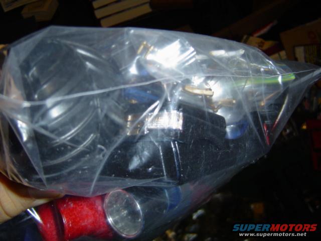 Plastic bag with various automotive parts, including red and silver tubing