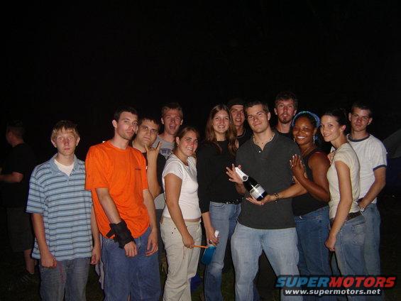 Group of young adults posing for a photo at night, one person holds a bottle of champagne