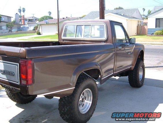 Brown Ford pickup truck, lifted with large tires, seen from rear quarter angle