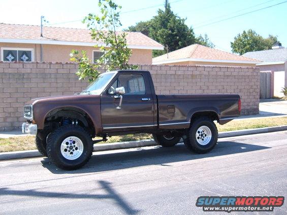 Brown pickup truck with lifted suspension and chrome wheels, parked on a street
