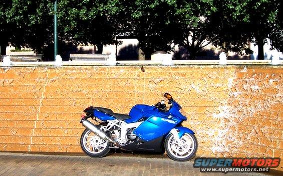 Blue BMW motorcycle parked by a brick wall with a fountain