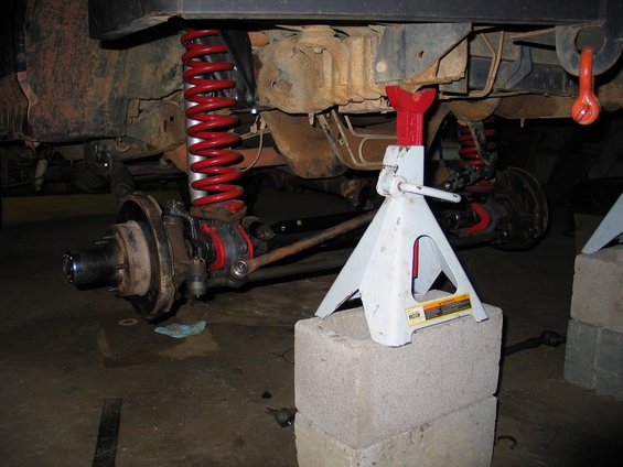 close-up of vehicle's front suspension with red coilover and white jack stand supporting the frame