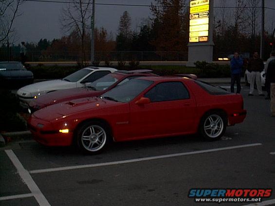 Red 1988 Mazda RX-7 parked next to a white car and a dark car