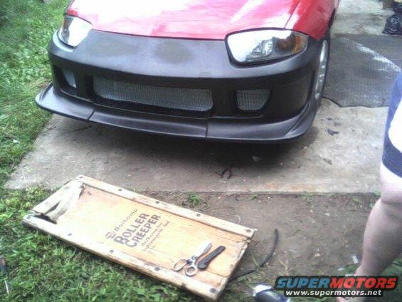 red car with black aftermarket bumper and mesh grille, roller creeper on ground