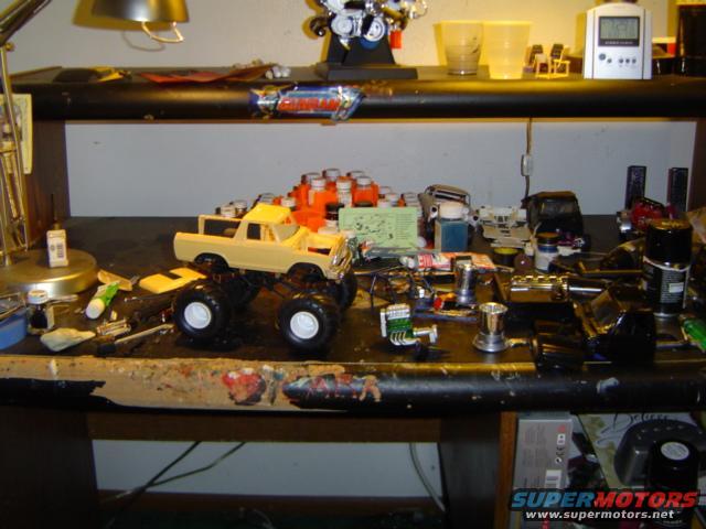 Yellow 1979 Ford Bronco model with large tires on a cluttered workbench