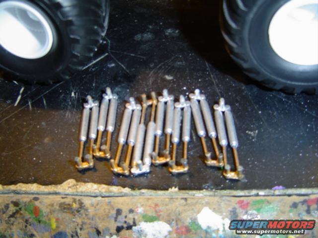 Several model car shock absorbers laid out on a black surface, with parts of two large tires visible at the top