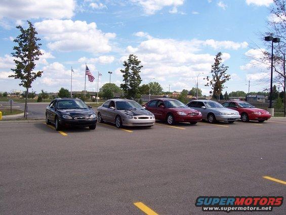 Five sedans parked in a lot, including a black 1998 Mercury Sable and a silver one