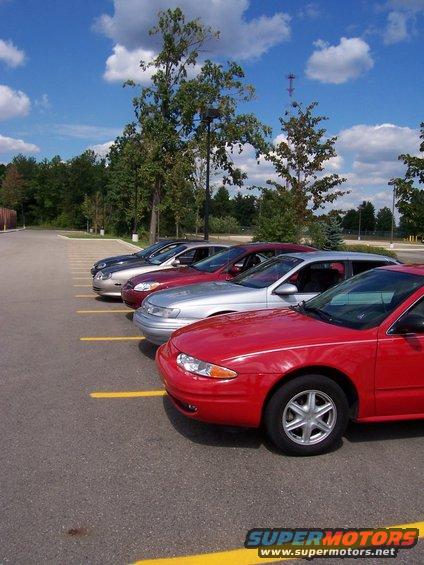 Several cars parked in a lot, red car in foreground