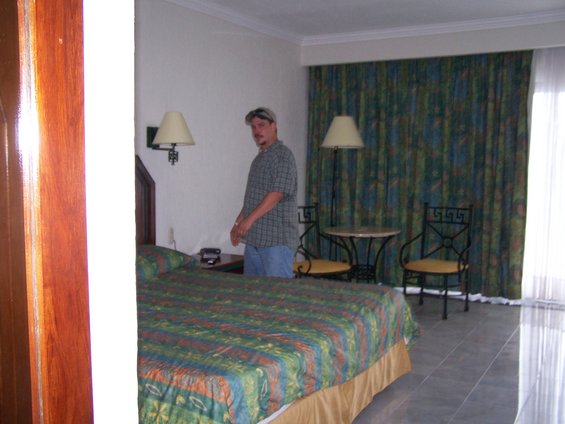 Hotel room with a bed, a man standing, and patterned curtains