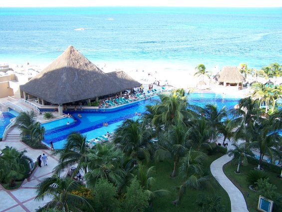 Resort with a large thatched-roof bar and pool overlooking a sandy beach and blue ocean