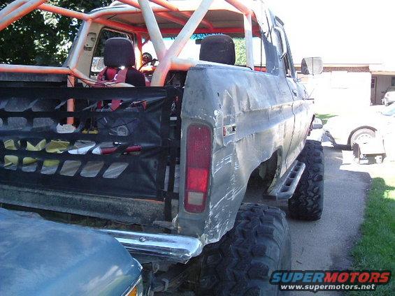 1979 Ford Bronco with extensive body damage, roll cage, and large tires, viewed from the rear