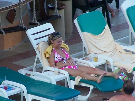 Woman in pink and white bikini on a white lounge chair with a yellow towel and sunglasses