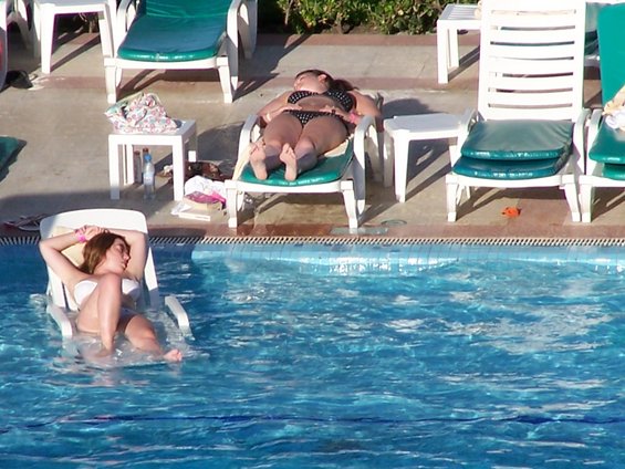 Two women relaxing on lounge chairs by a swimming pool