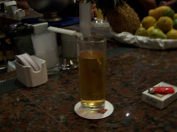 Bar counter with a glass of amber liquid on a coaster, a pack of Marlboro cigarettes, and a red lighter