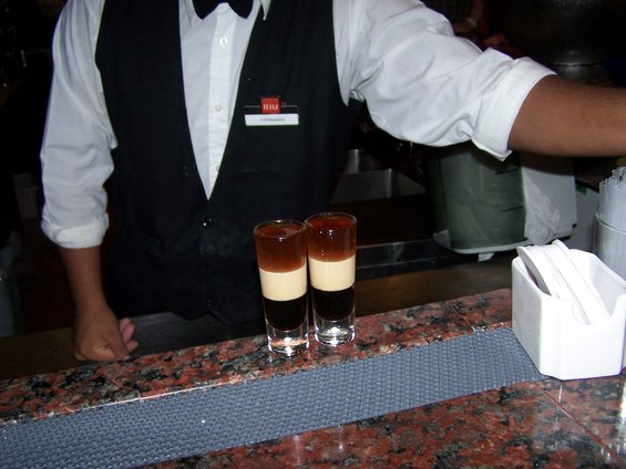 bartender in uniform with two layered shots on a granite bar top