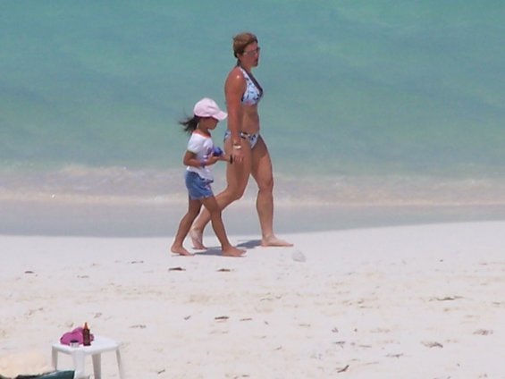 Woman and child walk on a sandy beach with turquoise water
