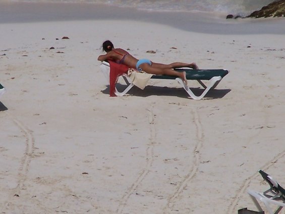 Woman in bikini lying on a lounge chair on a sandy beach with the ocean in the background
