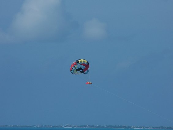 Colorful parasail in blue sky over ocean with distant shoreline