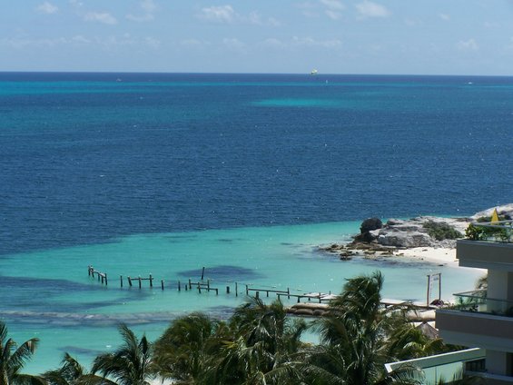 Ocean view with turquoise water, white sand beach, rocky outcroppings, and a dilapidated pier