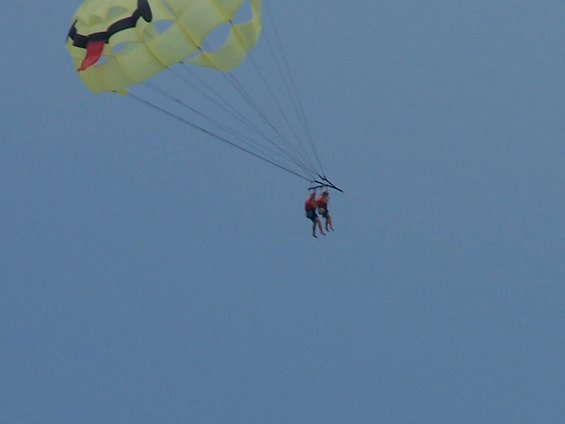 Two people parasailing under a yellow parachute with a smiley face design