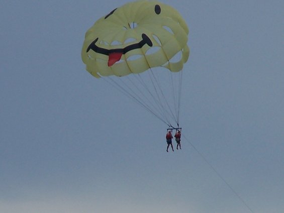 Yellow parasail with a smiley face and tongue sticking out, carrying two people