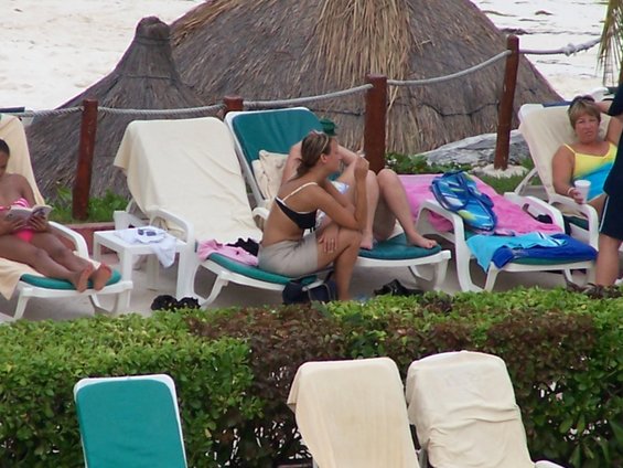 People in swimwear sit on lounge chairs near a beach with thatched umbrellas