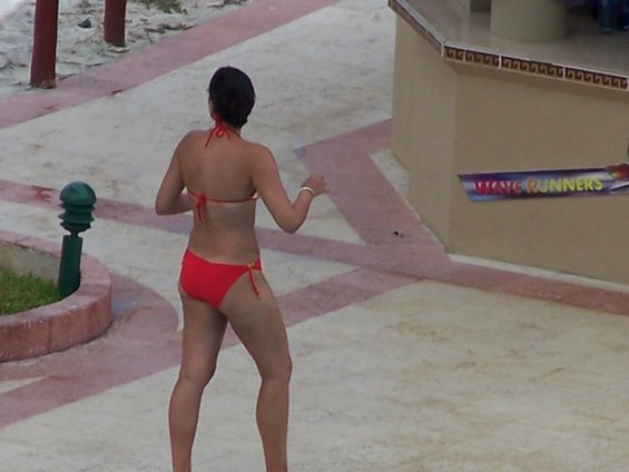 Woman in red bikini from behind, standing on a paved area with sand in the background. A sign reads WAVE RUNNERS
