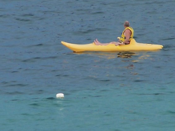 Man wearing a yellow life vest sits in a yellow kayak on the water