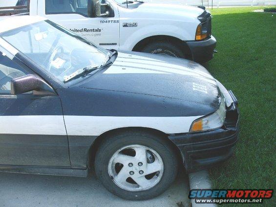 Dark blue and white car with a white stripe, parked next to a white truck. Front wheel and hood visible