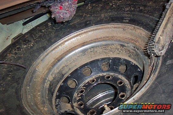 Mud-caked tire and black steel wheel with multiple lug nuts, close-up view