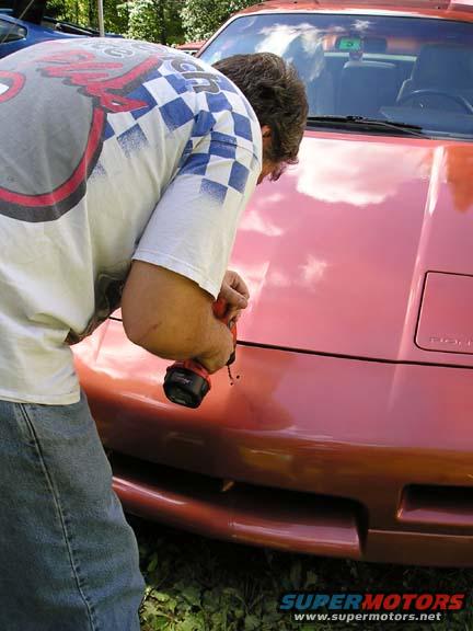 Man with drill working on the hood of a red 1984 Pontiac Fiero