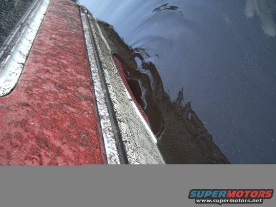 close-up of red and silver vehicle body panel with water on dark surface