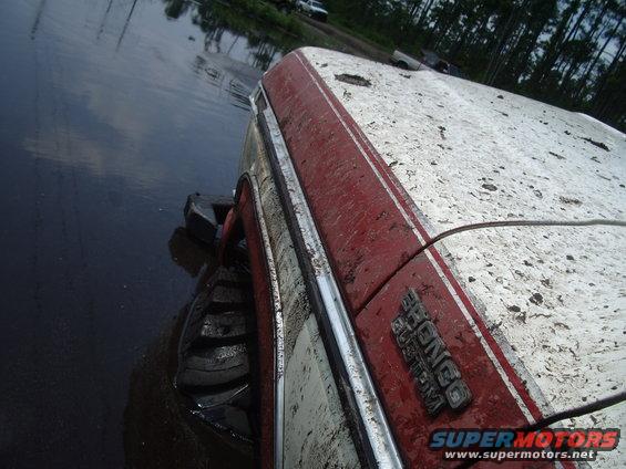Muddy 1978 Ford Bronco stuck in water, side view showing large tires