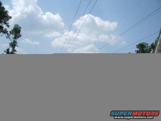 Partial view of a vehicle's side mirror and roofline against a cloudy sky