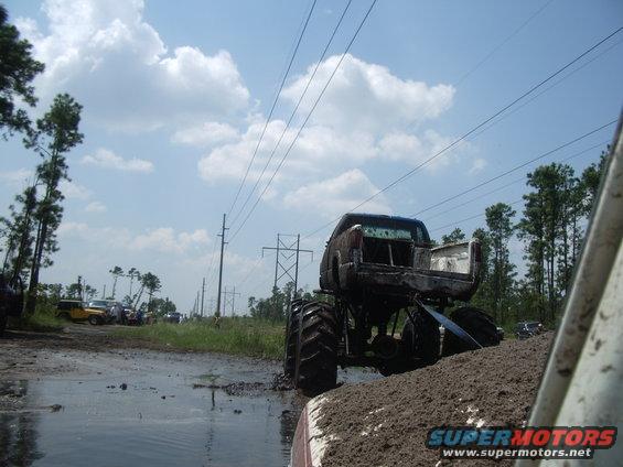 Monster truck with large tires stuck in mud, other vehicles visible in background