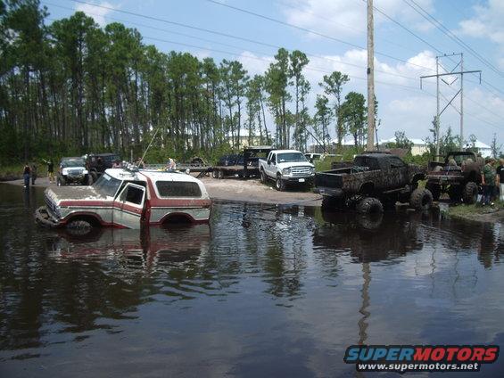 1978 Ford Bronco partially submerged in water with other trucks nearby
