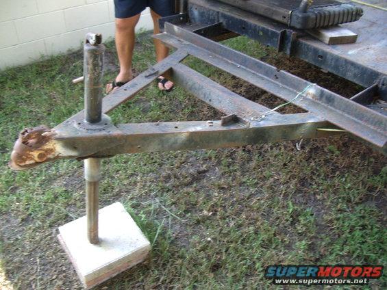 Trailer tongue with jack stand on concrete block, showing rusty coupler and metal frame