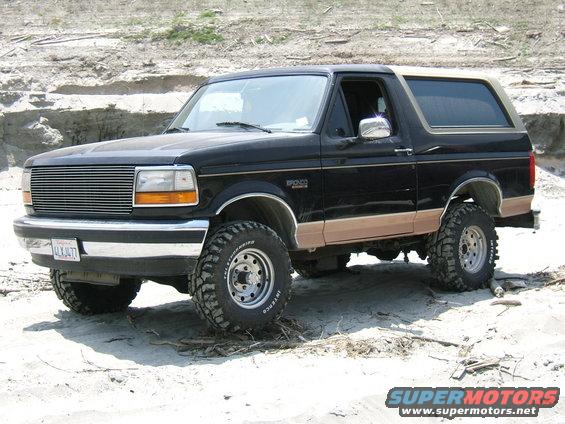 Black Ford Bronco with tan trim, lifted on off-road tires, parked on sandy terrain