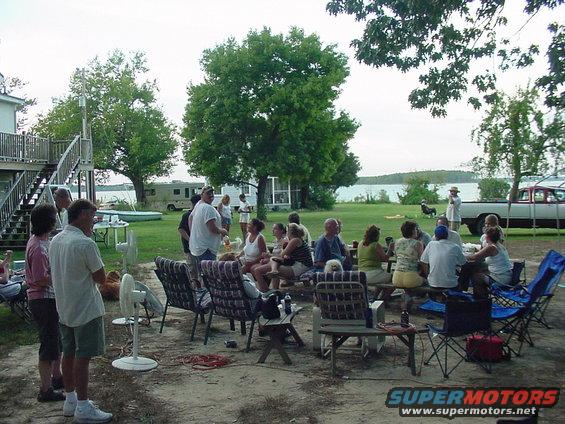 People gathered outside by a lake, with an RV and a pickup truck visible