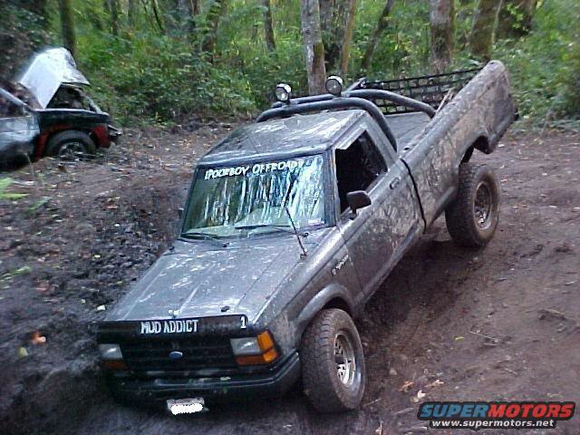 Mud-covered 1992 Ford Ranger pickup truck with off-road lights and a roll cage, stuck in mud