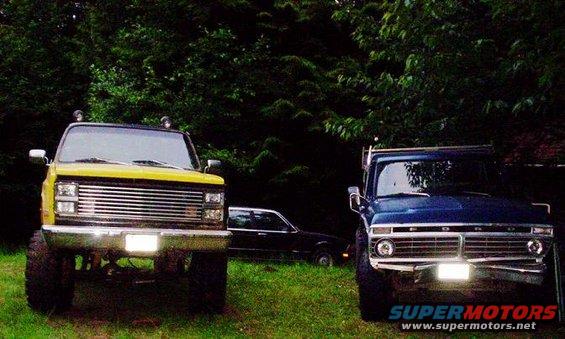Blue Ford pickup truck front view, with a yellow pickup and sedan behind