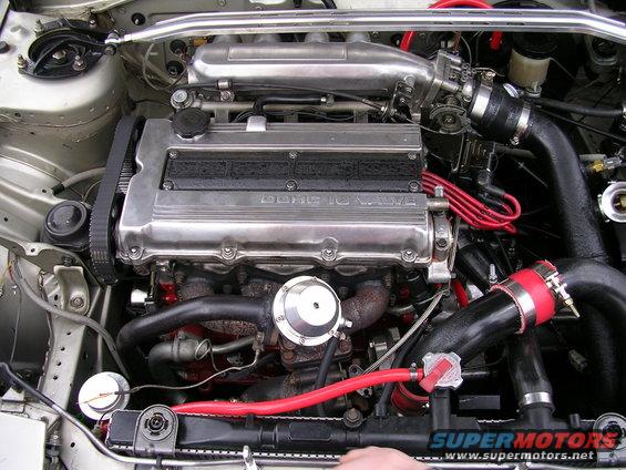 engine bay with DOHC 16 VALVE engine cover, red hoses, and black intake piping