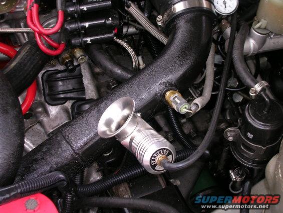 Engine bay showing a turbocharger intake pipe, blow-off valve, and various hoses and sensors. Text 'TURBOXS' visible on the valve