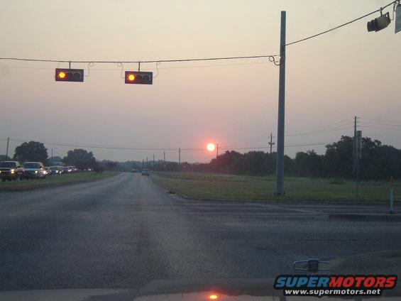 Sunrise over a road with traffic lights and cars in the distance