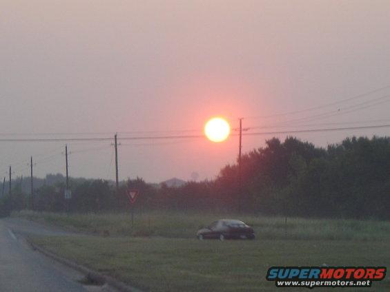 Dark sedan parked in a grassy field during a hazy sunrise, side view